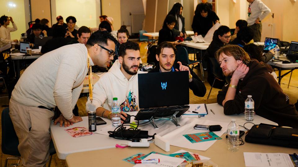 Four people gathered around a laptop screen at the Global Game Jam.
