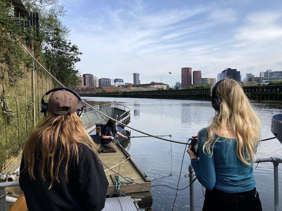 Three students conducting a sound recording by a river.