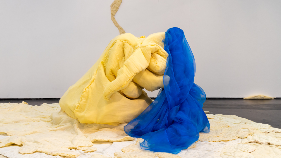 Two colourful sculptures in an exhibition space, one is yellow and the other is blue