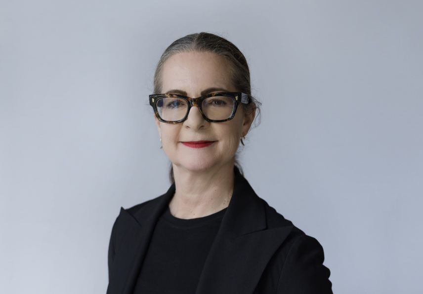 White female with black rectangular glasses and black outfit smiles for the camera.