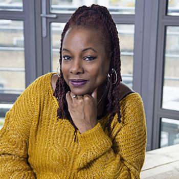 Graduate Kocoa wearing a yellow/gold jumper sitting in the Goldsmiths Students' Union