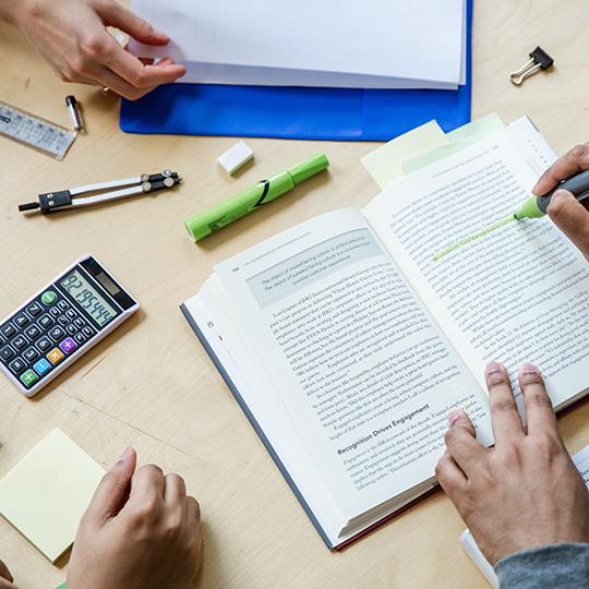 A group of students sitting around a book and calculators.